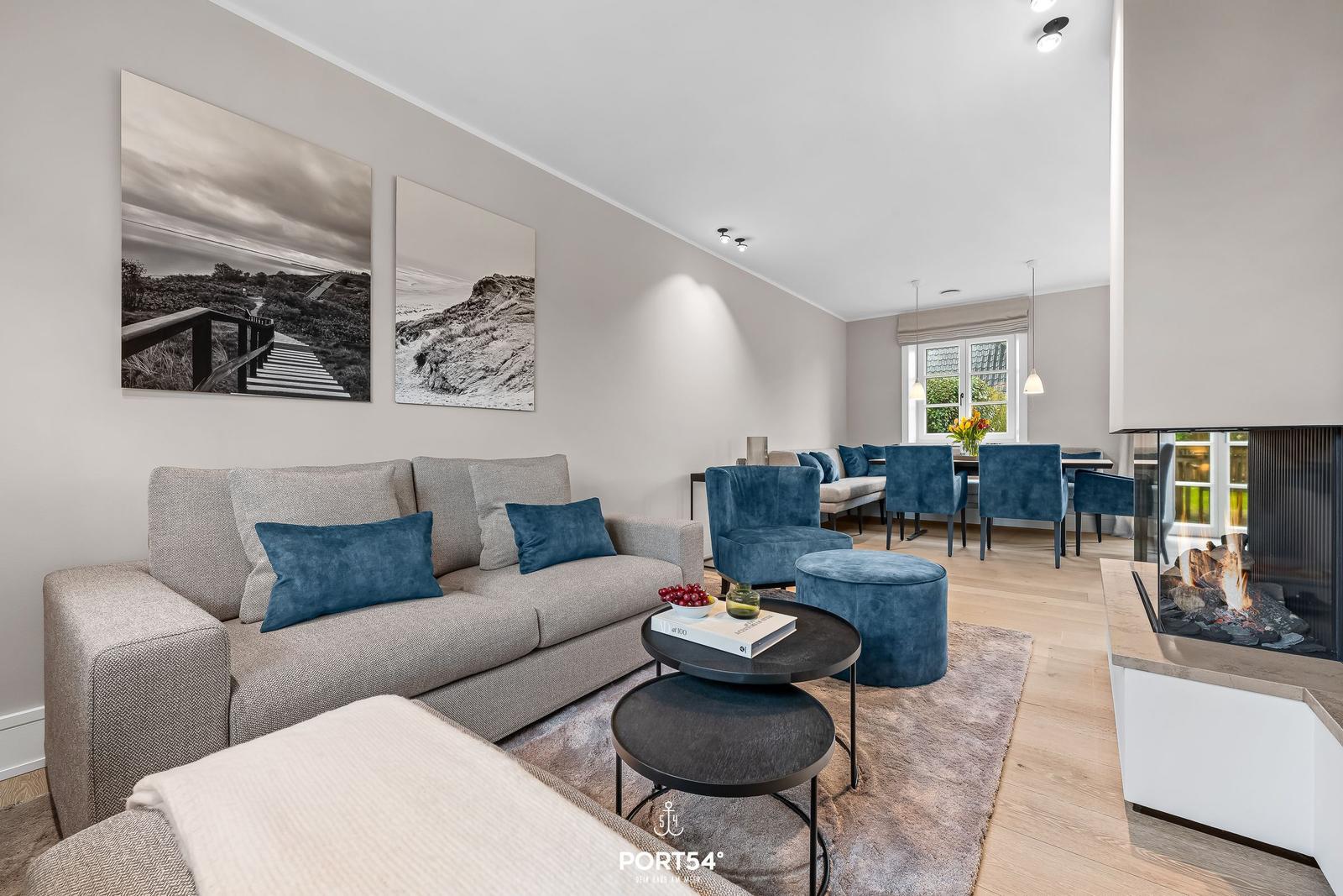 Wohn- und Essbereich mit Kamin, Sofa und blauen Sesseln.