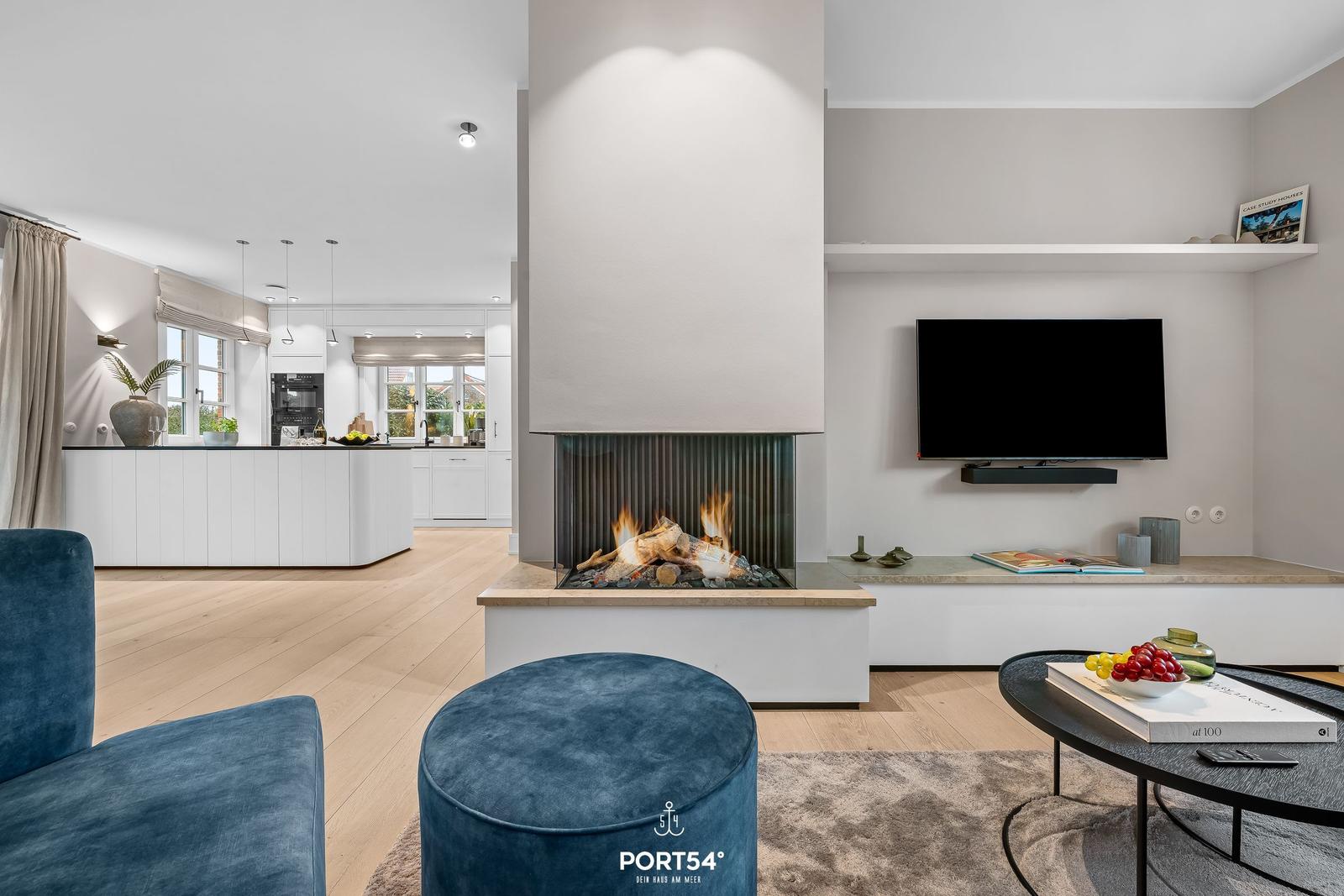 Wohnzimmer mit Kamin, Fernseher und Küchenbereich im Hintergrund.