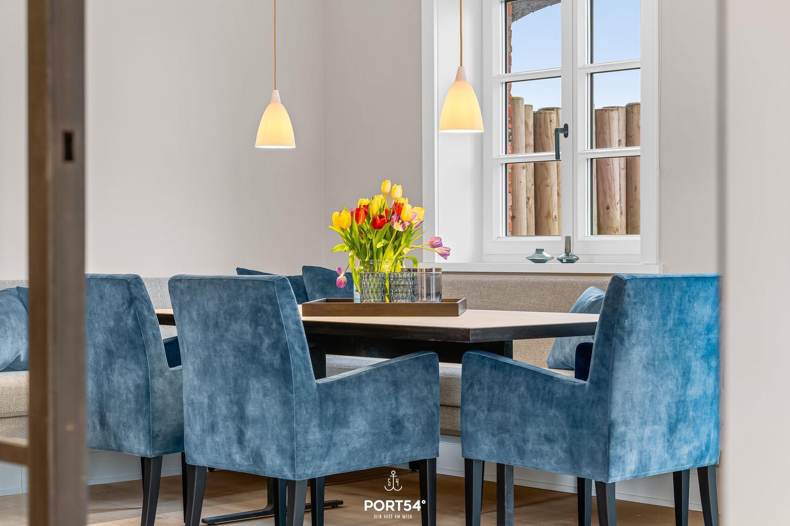 Esszimmer mit blauen Stühlen, Tisch und Blumen vor Fenster