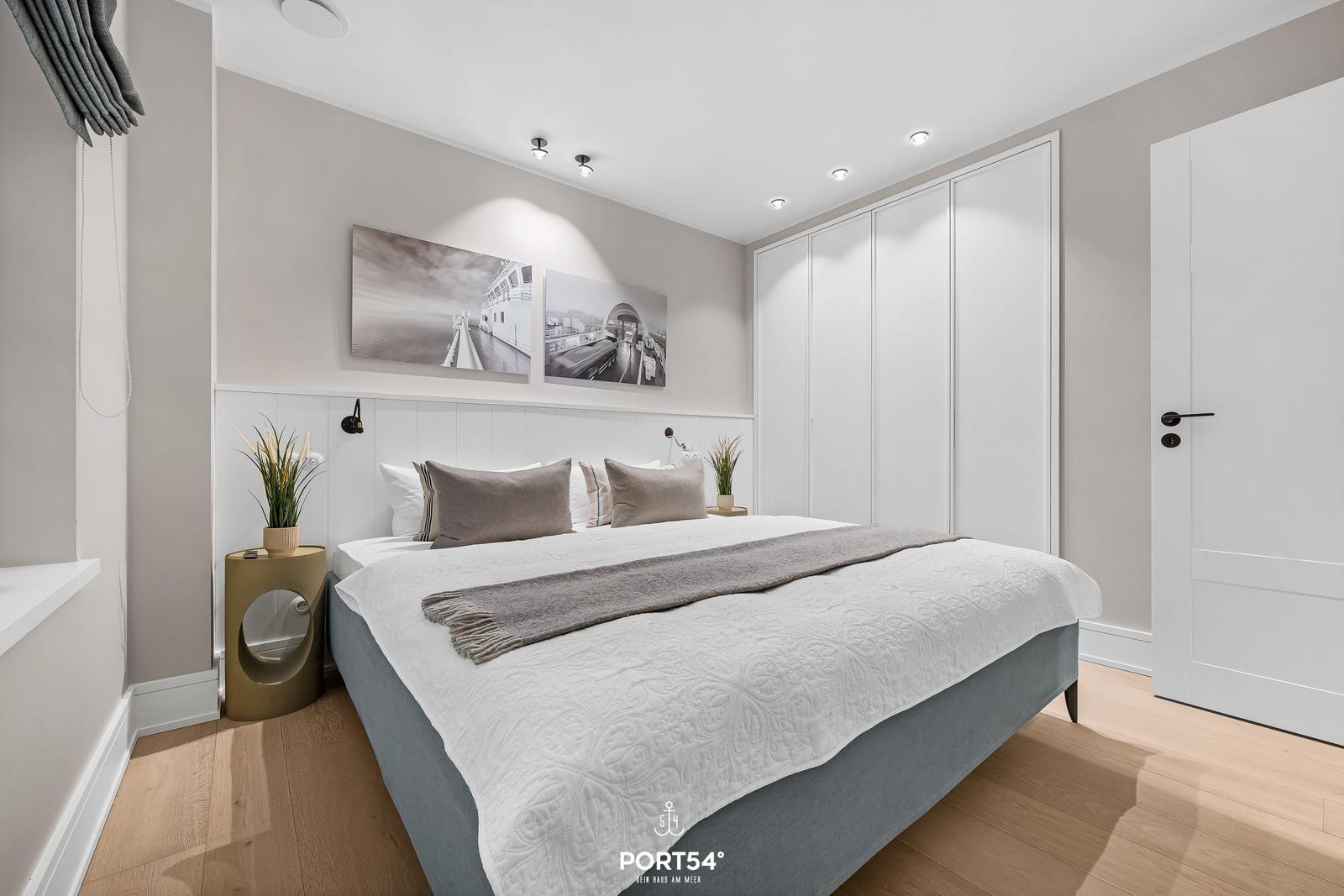 Schlafzimmer mit Bett, Kleiderschrank und Wandbildern.