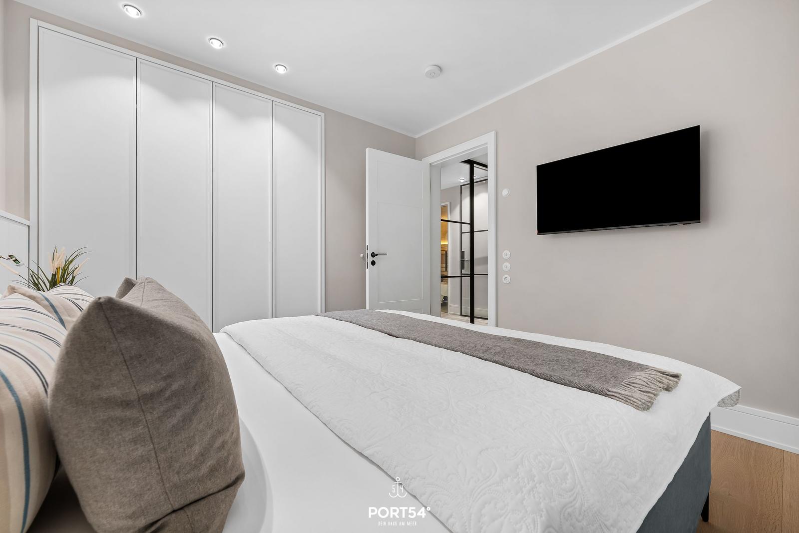 Schlafzimmer mit Bett, Kleiderschrank und Wandfernseher