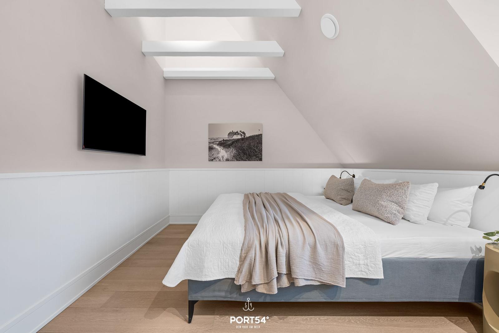 Schlafzimmer mit Dachschrägen, Bett, Wandbild und TV.