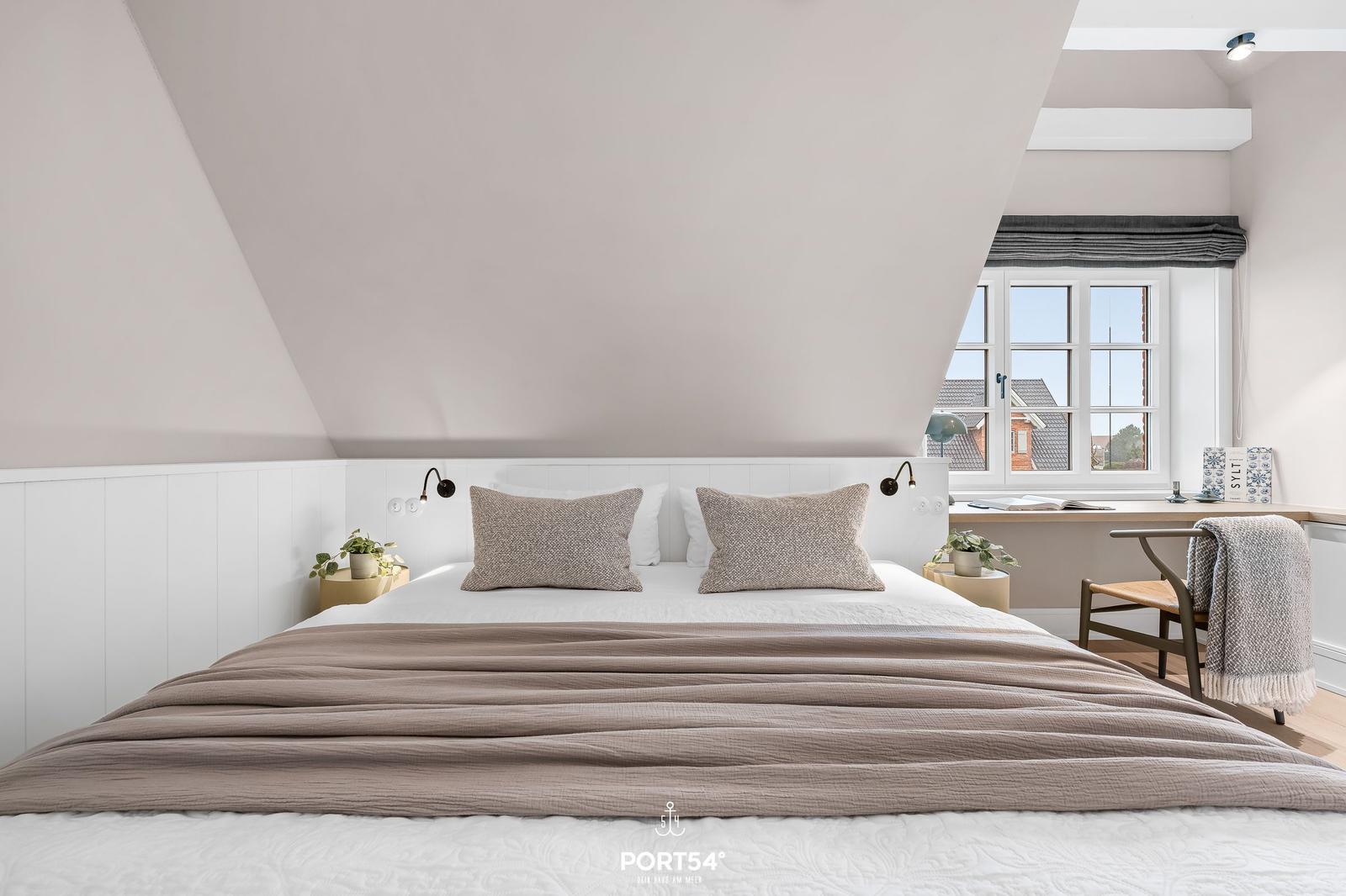 Schlafzimmer mit Dachschrägen, großem Bett und Fensterblick.