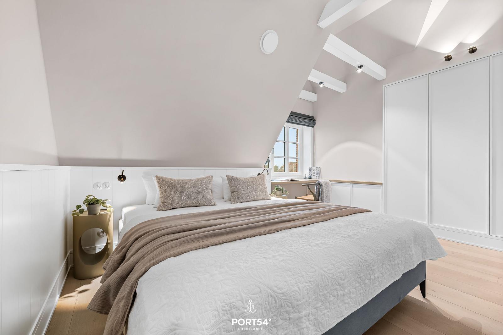 Schlafzimmer mit Dachschrägen, Bett, Schrank und Fenster.