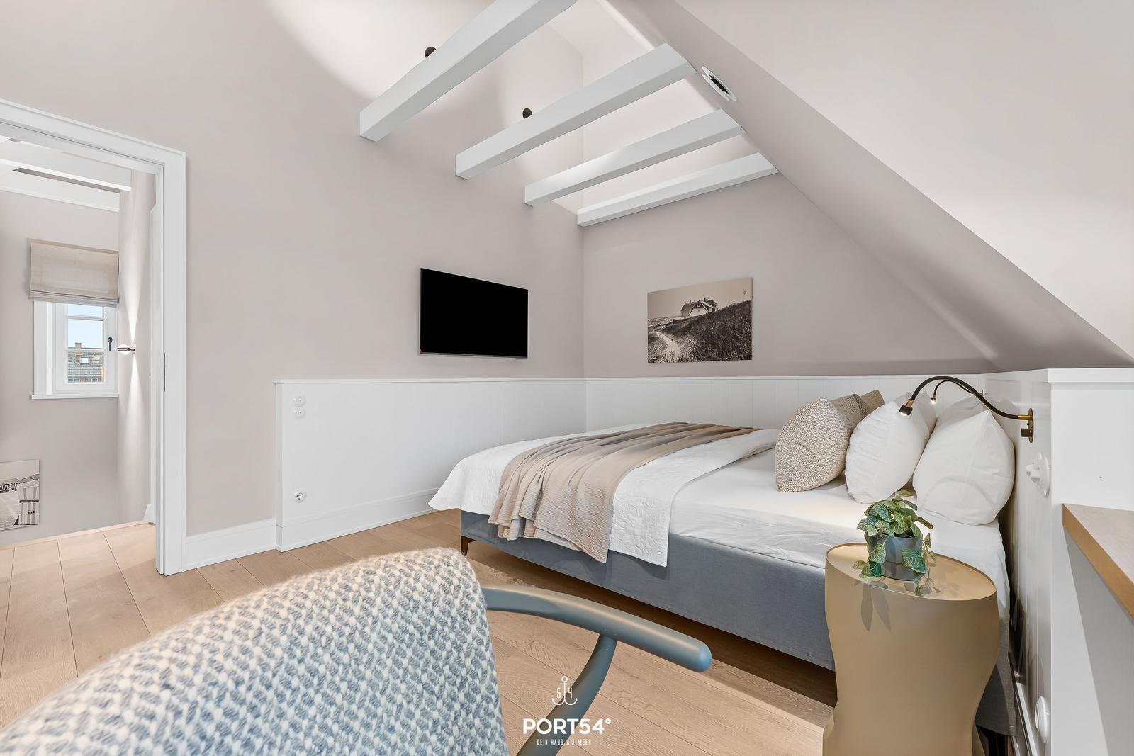 Schlafzimmer mit Dachschrägen, Bett, Fernseher und Pflanze.