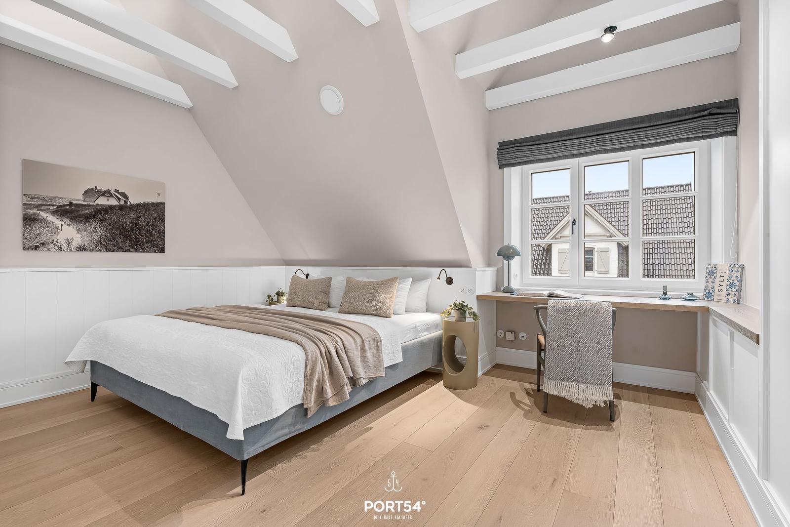 Schlafzimmer mit Dachschrägen, Bett, Schreibtisch und Fenster mit Blick.