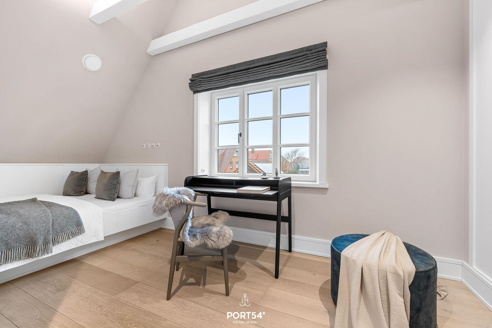 Schlafzimmer mit Dachschräge, Bett, Schreibtisch und Fenster.