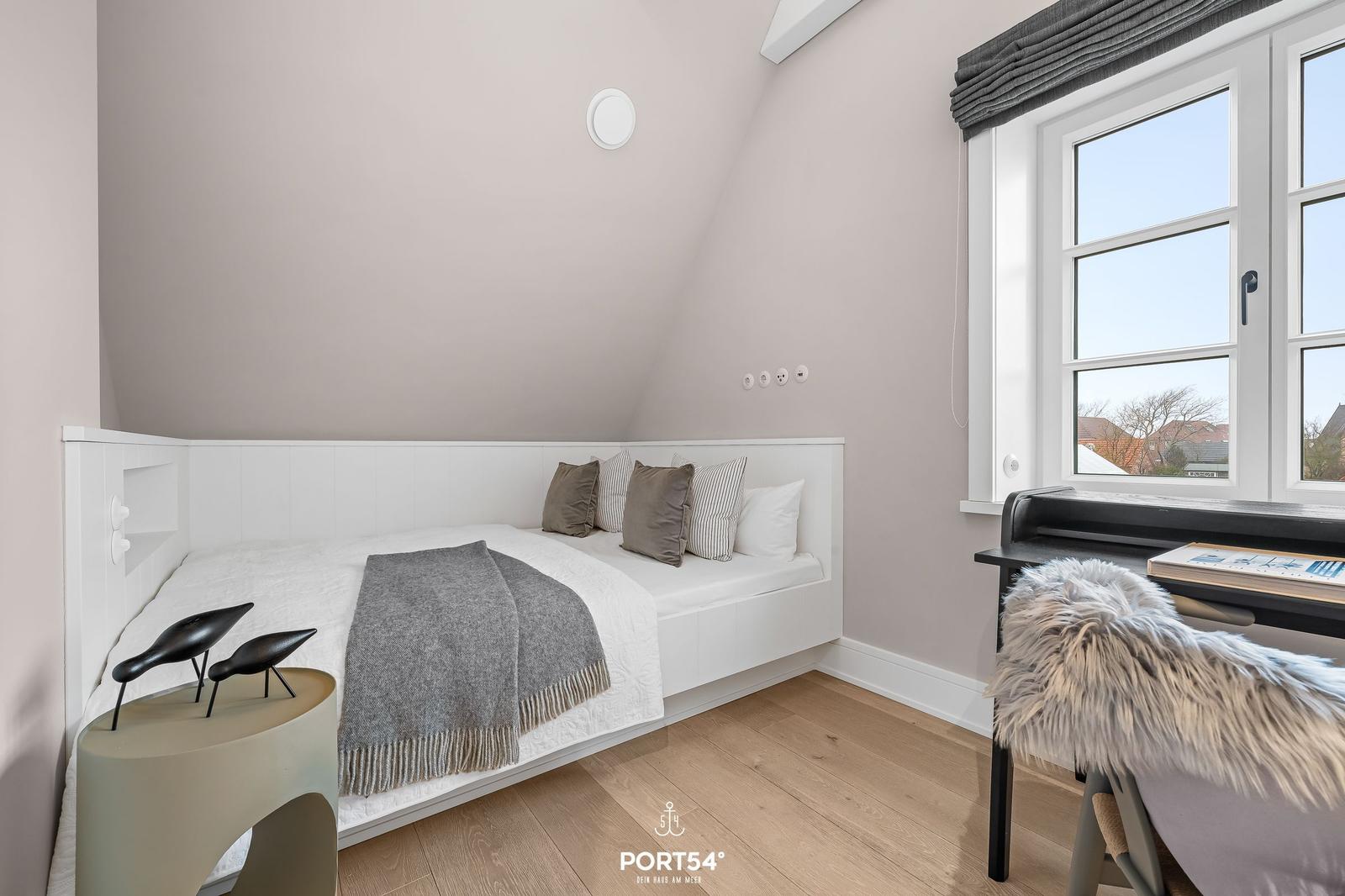 Schlafzimmer mit Dachschrägen, Bett, Schreibtisch und Fenster.