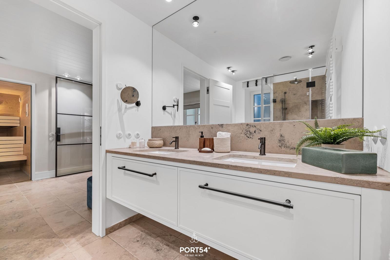 Badezimmer mit Doppelwaschbecken, Spiegel und Sauna im Hintergrund.