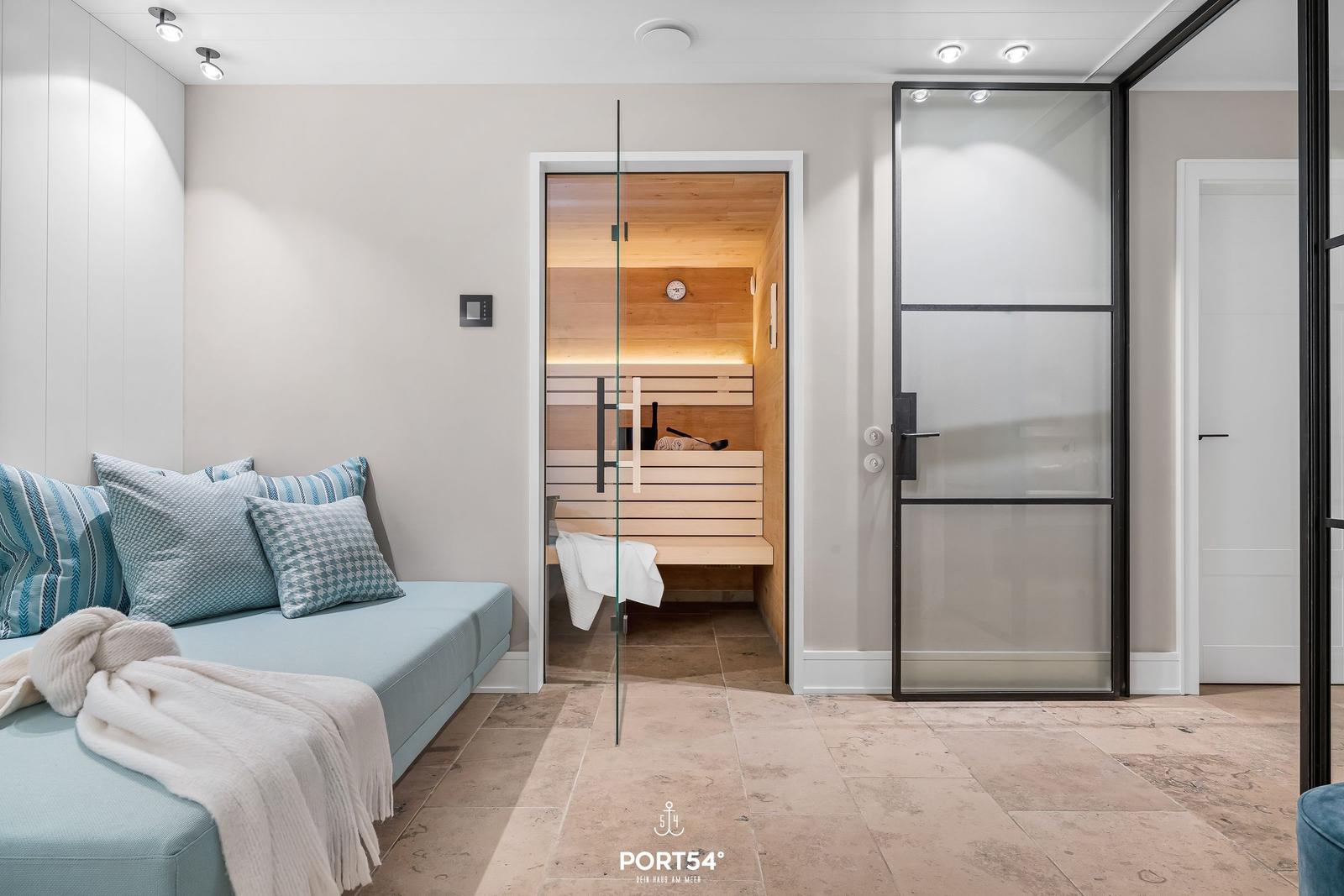 Sauna mit Holzbank und Glaswand. Sofa mit Kissen und Decke.