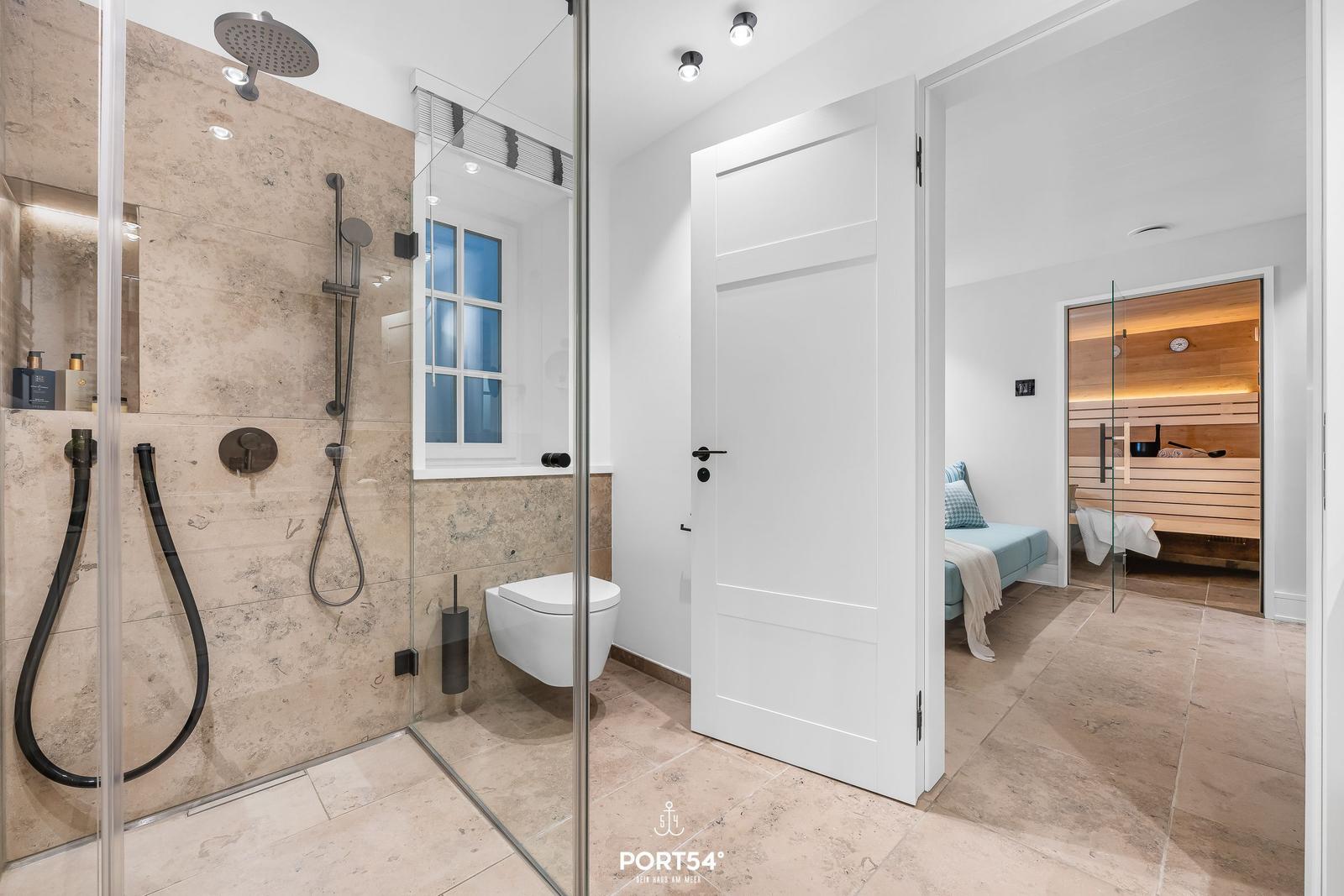 Dusche mit Duschbrause, Toilette und Blick in Schlafzimmer mit Sauna.