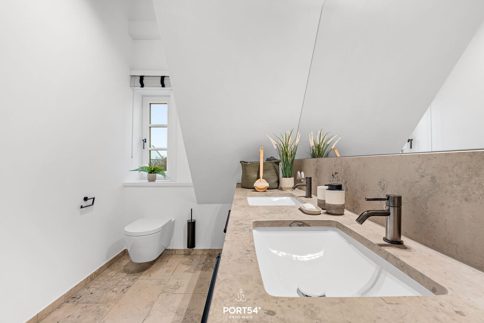 Badezimmer mit Doppelwaschbecken, Toilette und Fenster