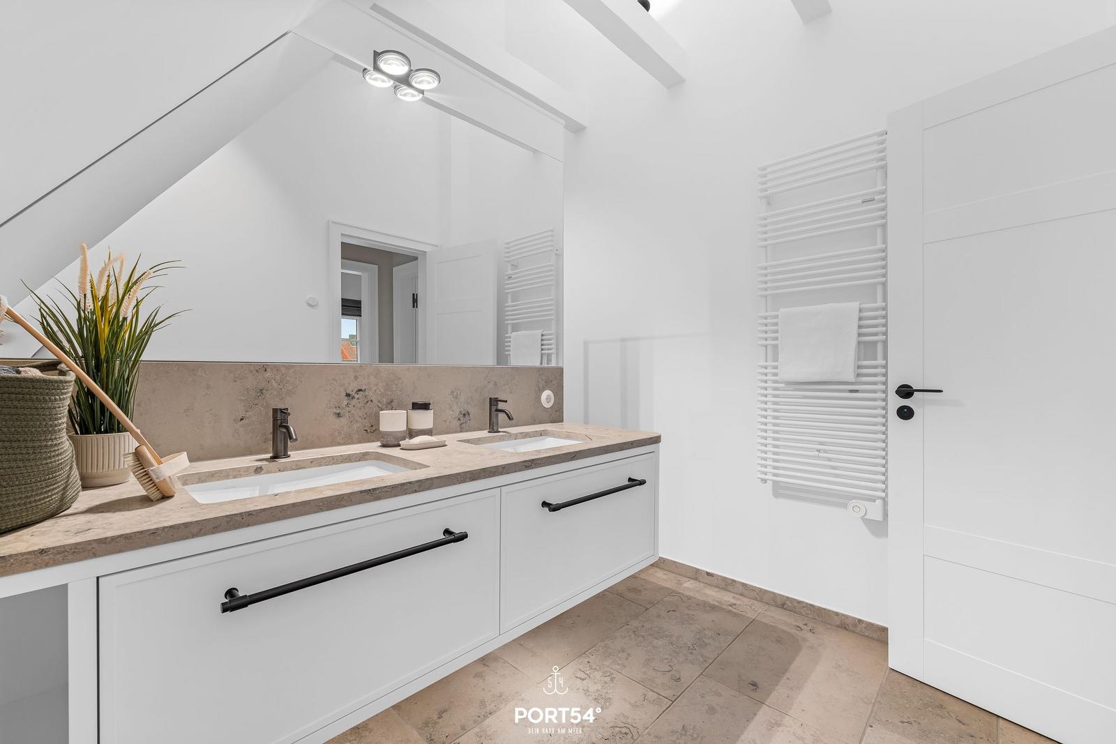 Doppelwaschbecken mit Spiegeln und Heizkörper an der Wand.