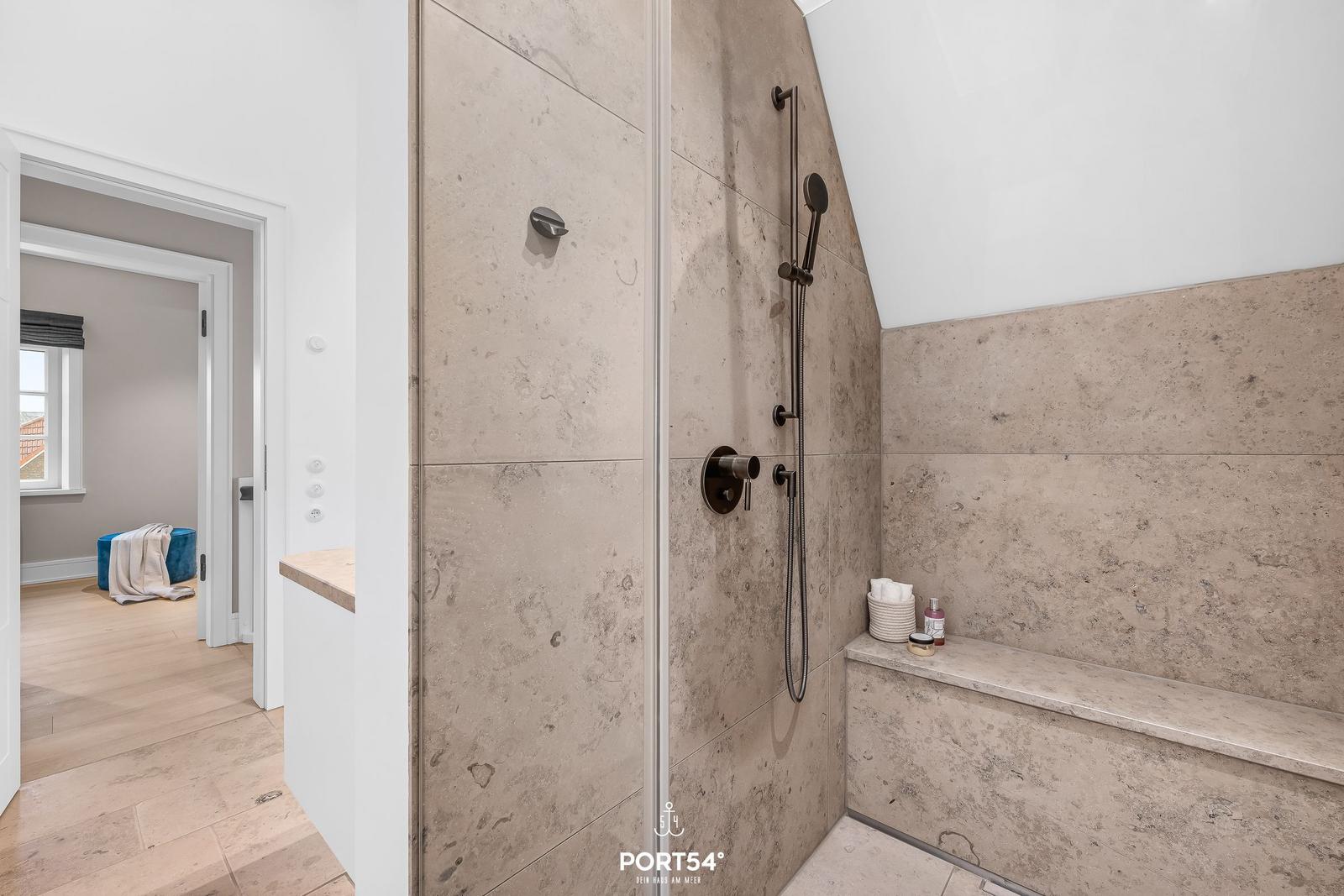 Dusche mit Steinwand und Sitzbank. Blick in angrenzenden Raum.