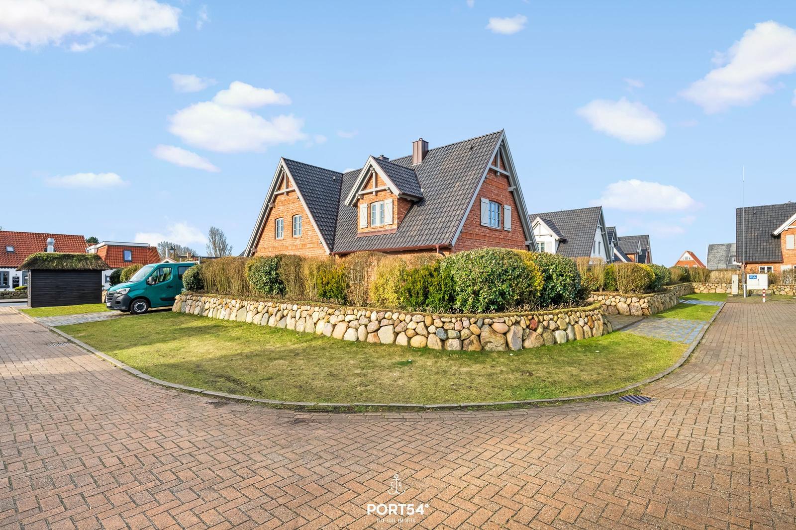 Rotes Backsteingebäude mit Steinmauer und Rasenfläche. Parkplatz mit grüner Van.
