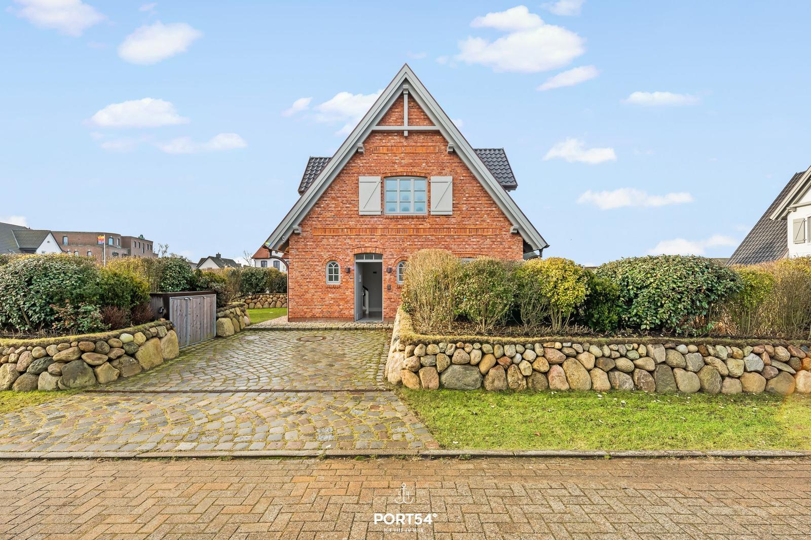 Rotes Backsteingebäude mit Steinmauer und Kiesweg. Eingangstür offen. Hinterhof mit Grünflächen.