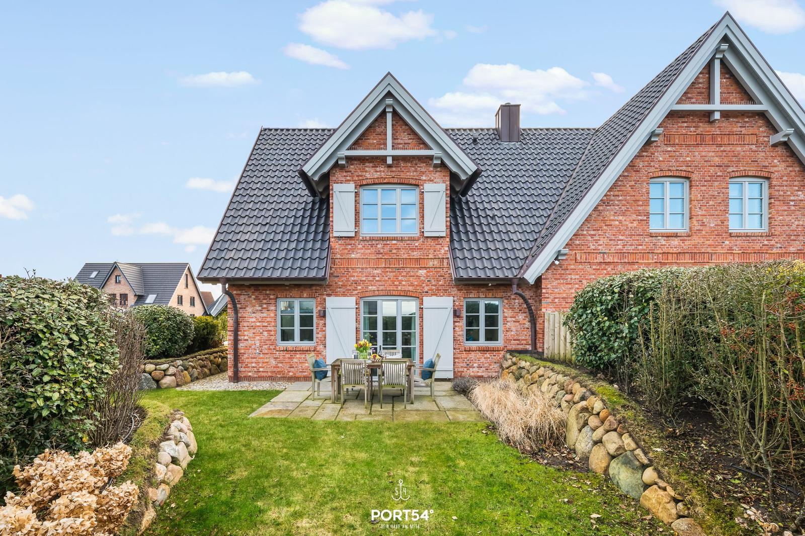 Rotes Backsteingebäude mit Garten und Terrasse. Holztisch und Stühle stehen draußen.