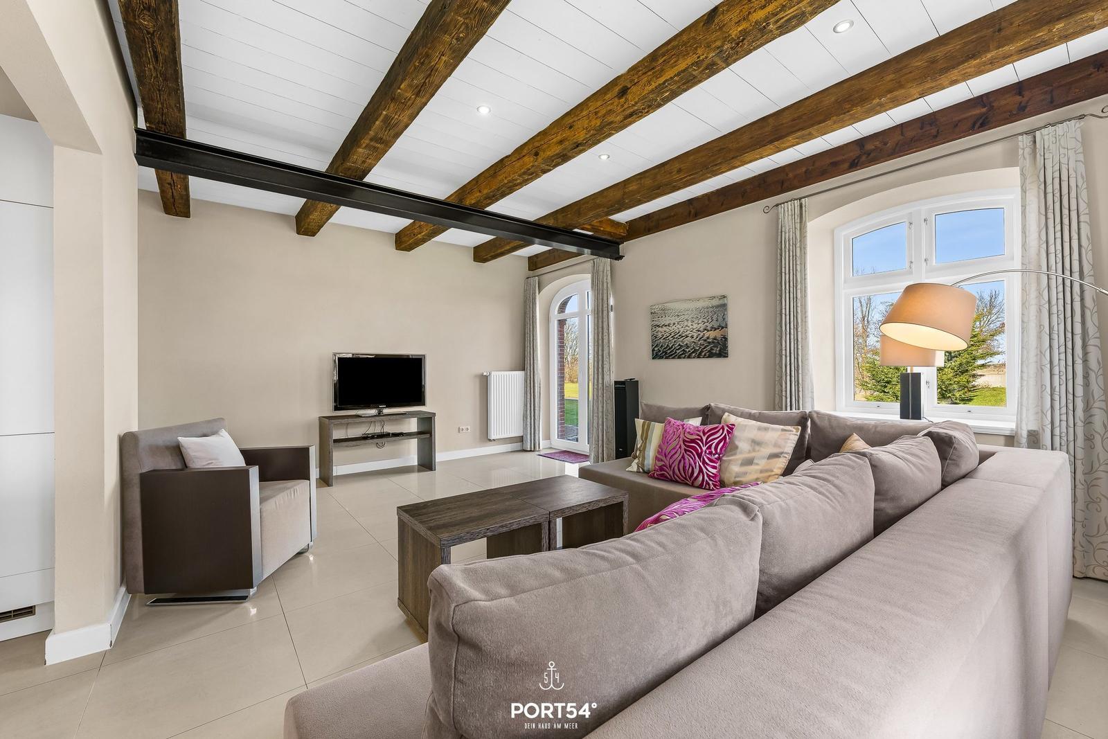 Wohnzimmer mit Sofa, Fernseher und Holzbalken an der Decke.