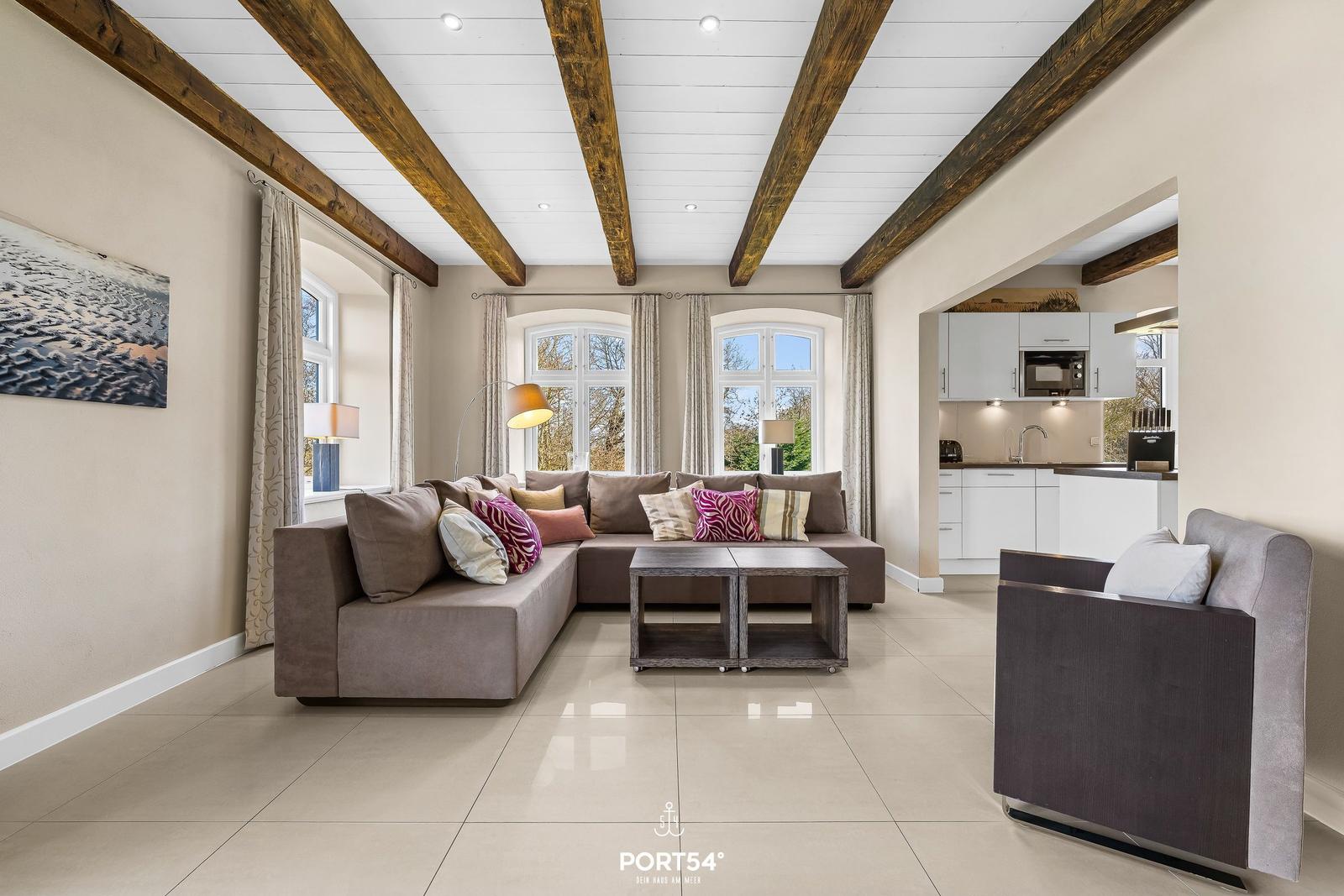 Wohnzimmer mit Ecksofa, Holzbalken und Küchenbereich im Hintergrund.