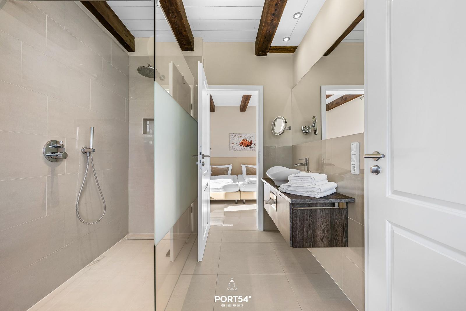 Badezimmer mit Dusche, Waschbecken und Blick in Schlafzimmer.