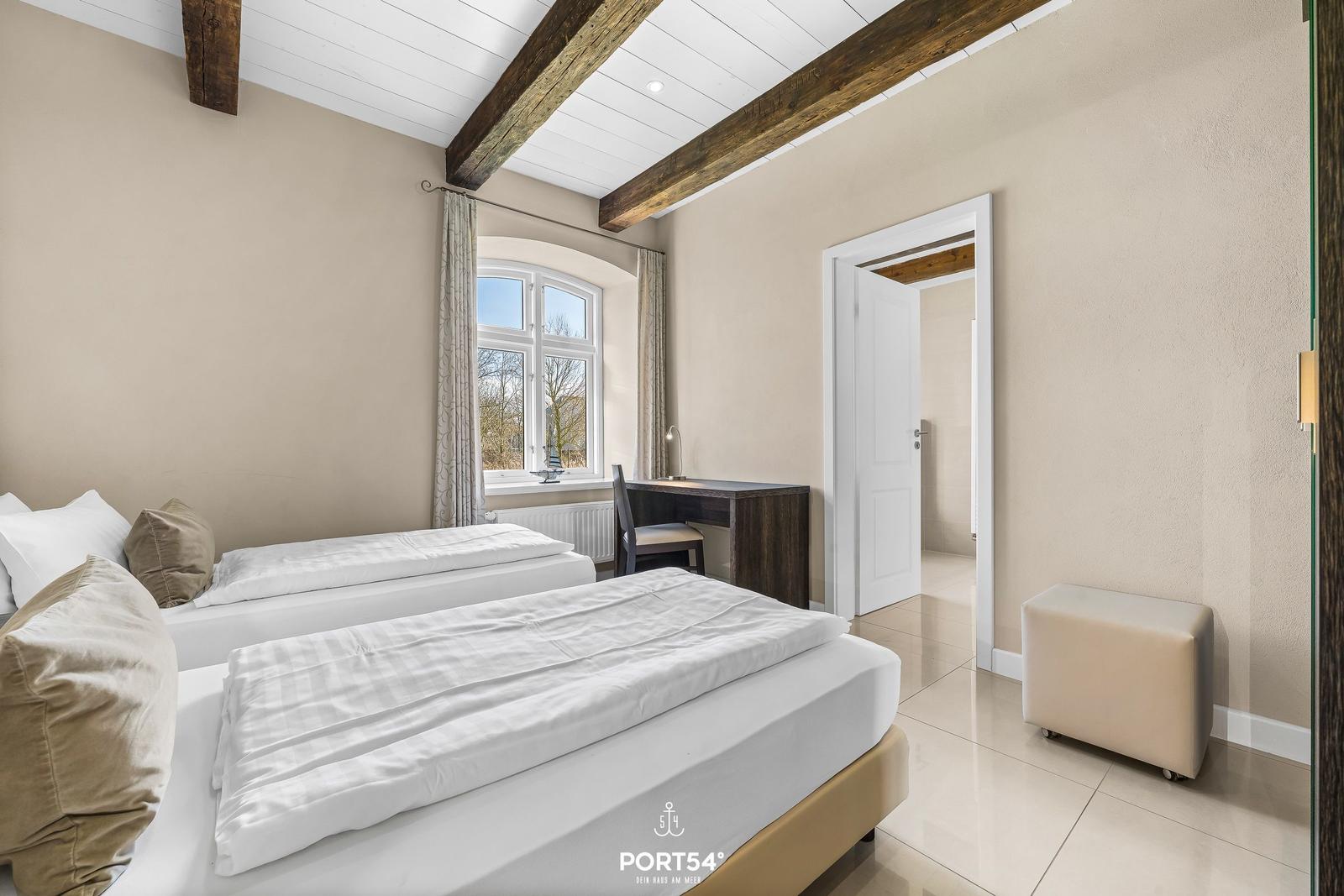 Zwei Betten, Schreibtisch und Fenster mit Blick. Holzbalken an Decke.