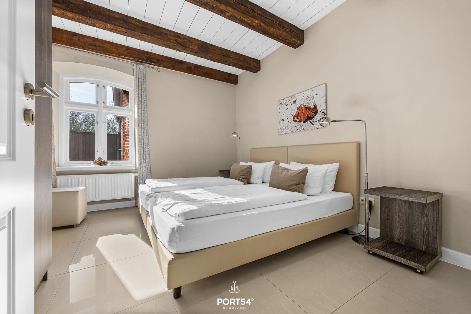 Schlafzimmer mit Doppelbett, Holzbalken und Fenster mit Blick nach draußen.