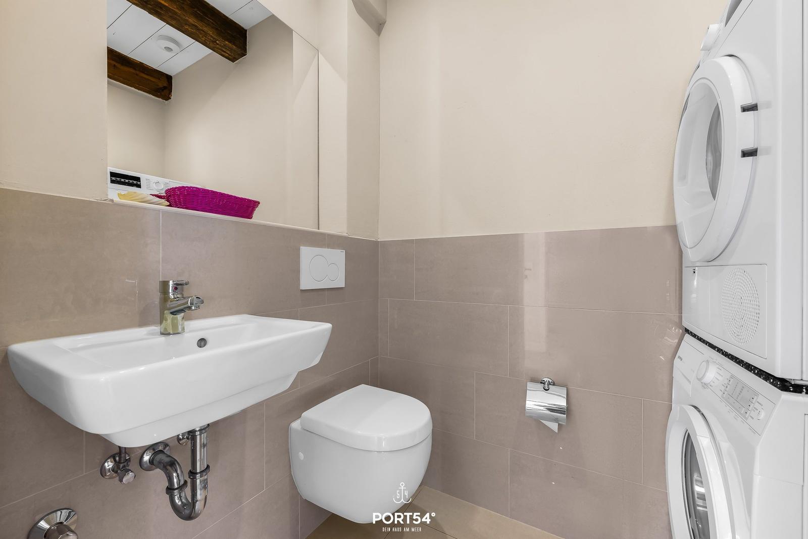 Badezimmer mit Waschbecken, WC und Waschmaschine-Trocknerkombination.