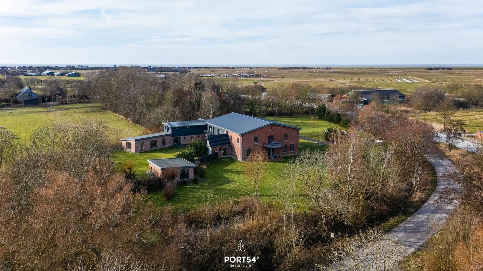 Rotes Haus mit moderner Anbauten auf grünem Grundstück mit Blick auf Felder und Horizont.