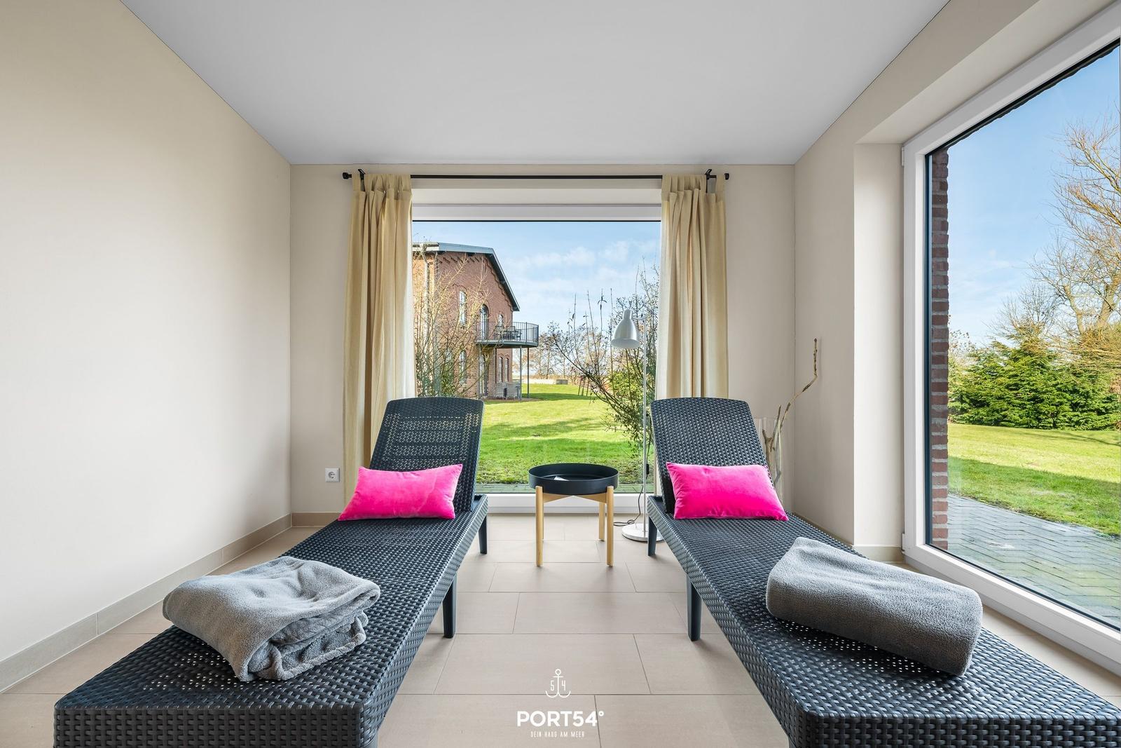 Zwei Liegestühle mit Kissen und Handtüchern vor großen Fenstern mit Blick auf Garten und Haus.
