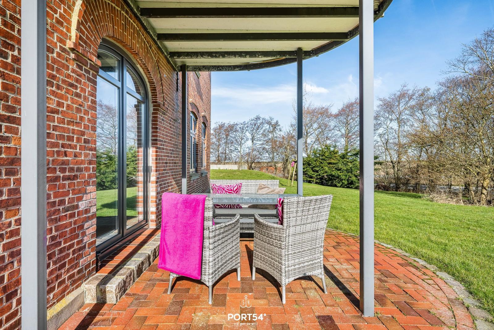Terrasse mit Sitzgruppe, pinkem Handtuch und Blick auf grünen Garten.