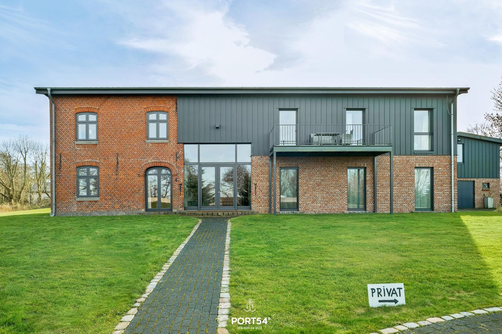 Moderne Villa mit Backsteinfassade und Balkon. Grünflächen und Weg zur Eingangstür.