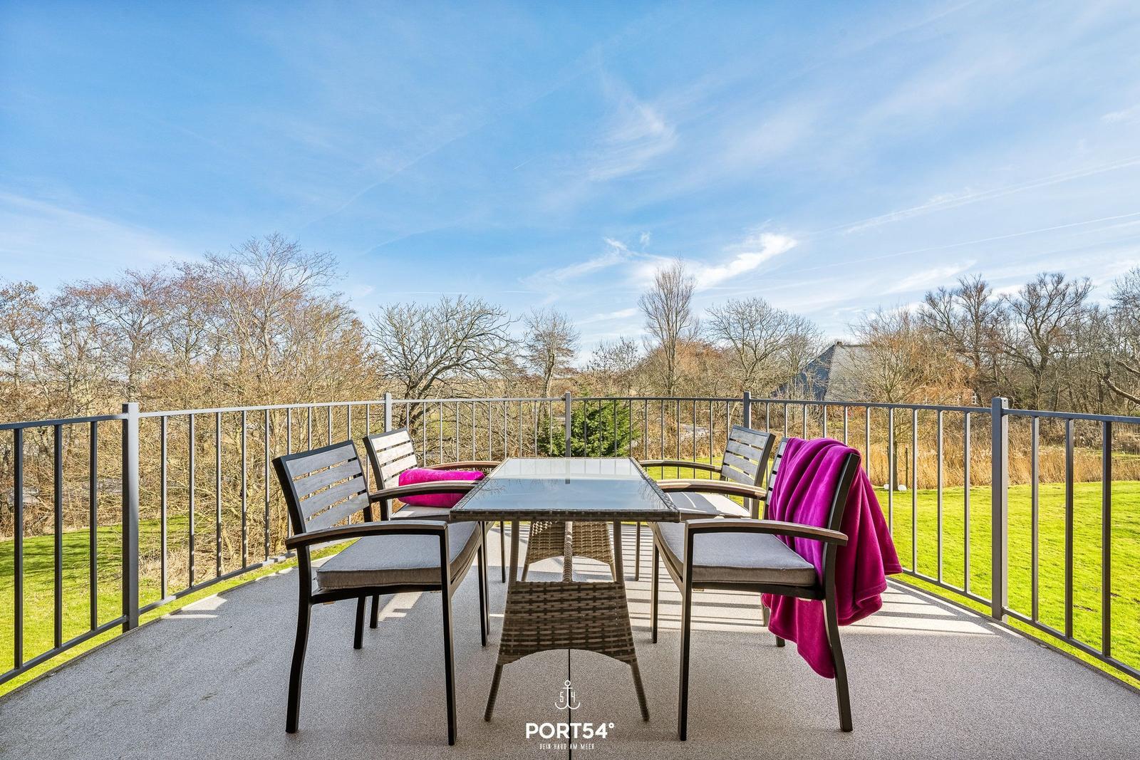 Terrasse mit Tisch und Stühlen, Blick auf Grünfläche und Bäume.