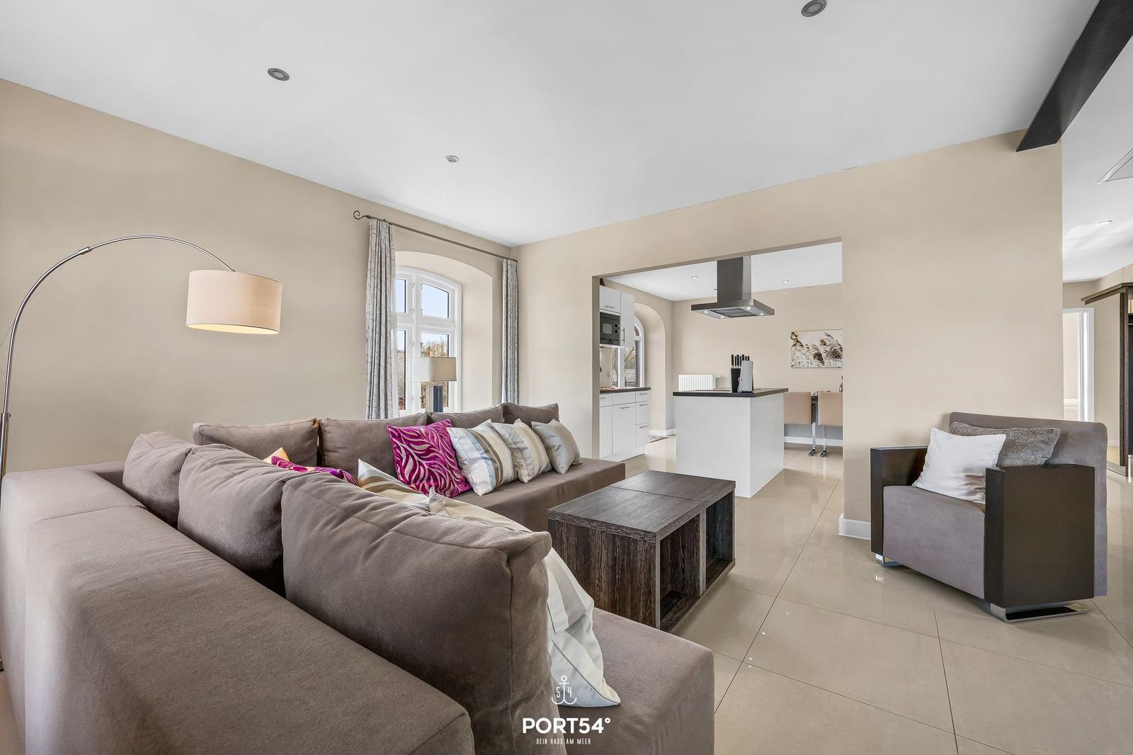 Wohnzimmer mit Sofa, Sessel und Küchenbereich im Hintergrund.