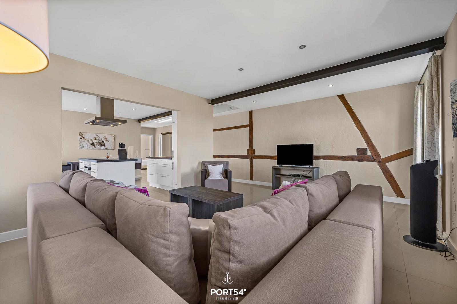 Wohnzimmer mit Sofa, Fernseher und Küchenbereich im Hintergrund.