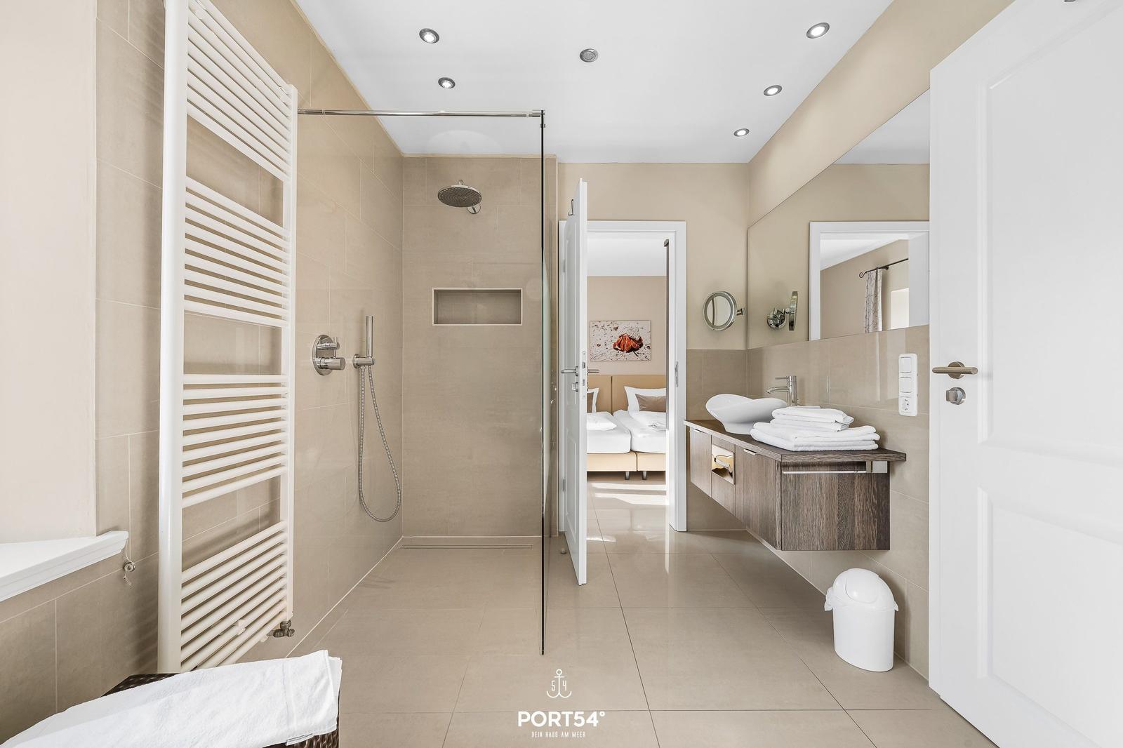 Badezimmer mit Dusche, Waschtisch und Blick in Schlafzimmer