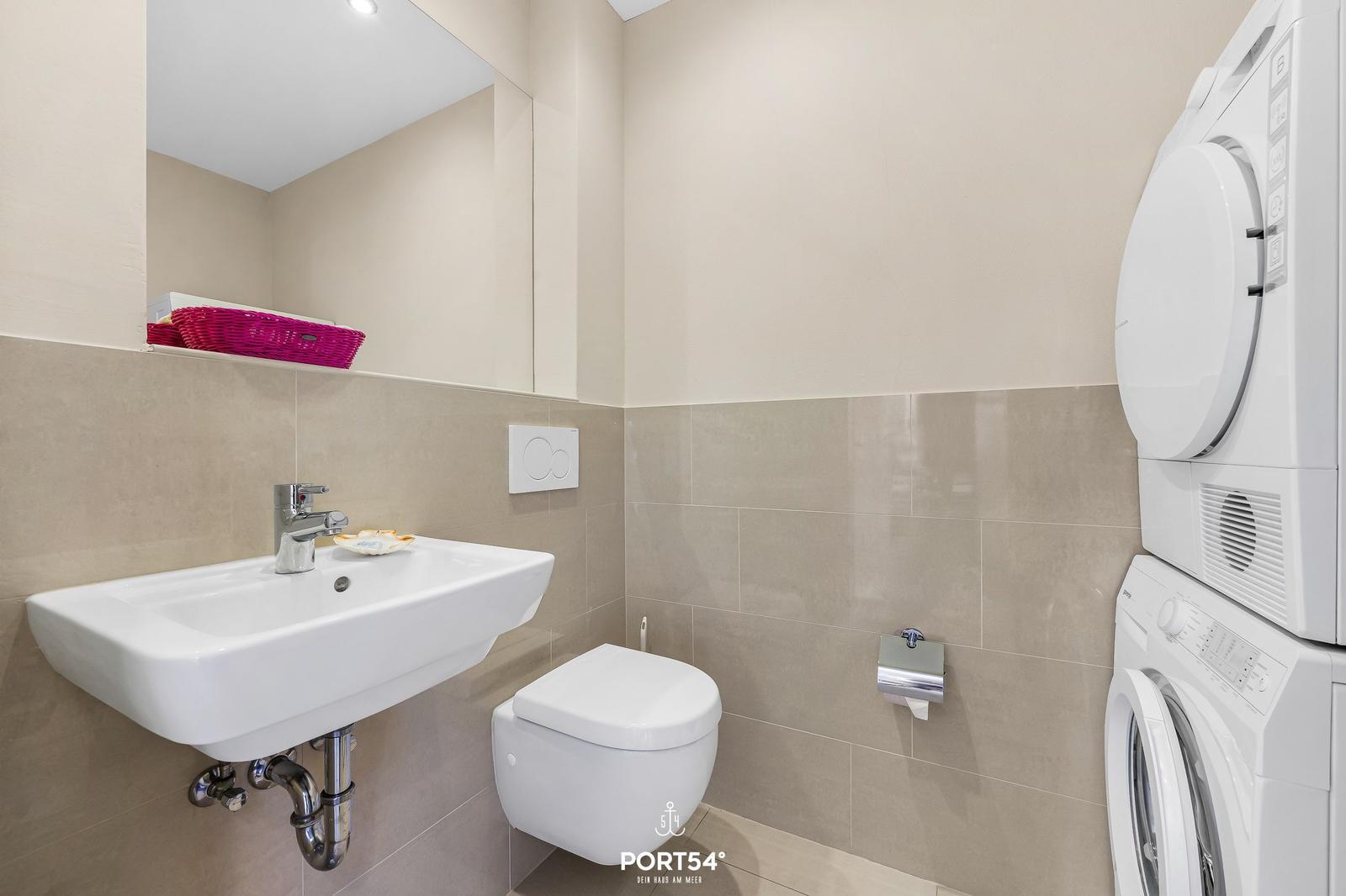 Badezimmer mit Waschbecken, Toilette und Waschmaschine-Trockner-Kombination.
