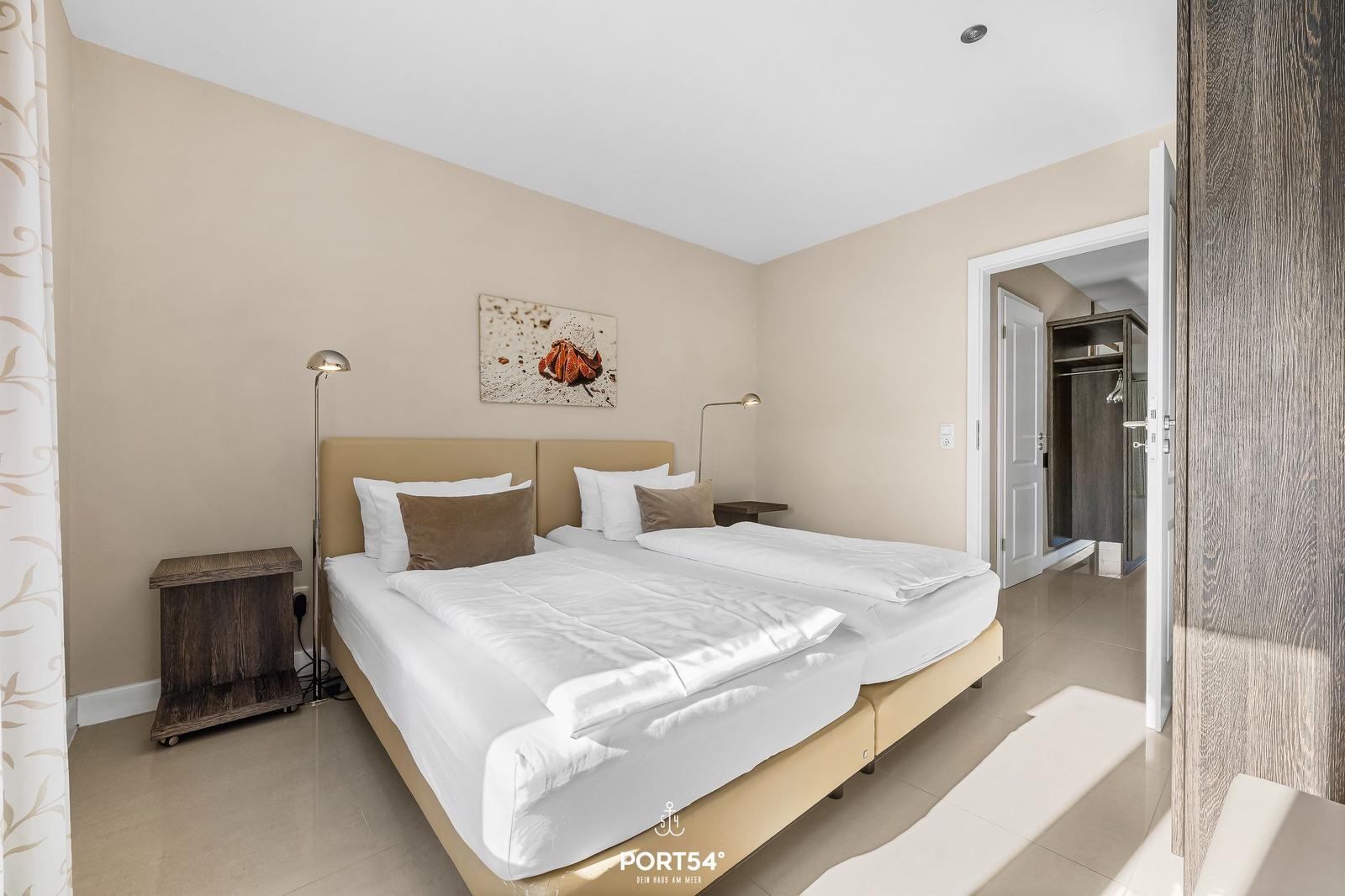 Schlafzimmer mit Doppelbett, Nachttischen und Wandbild. Tür führt zum Bad.