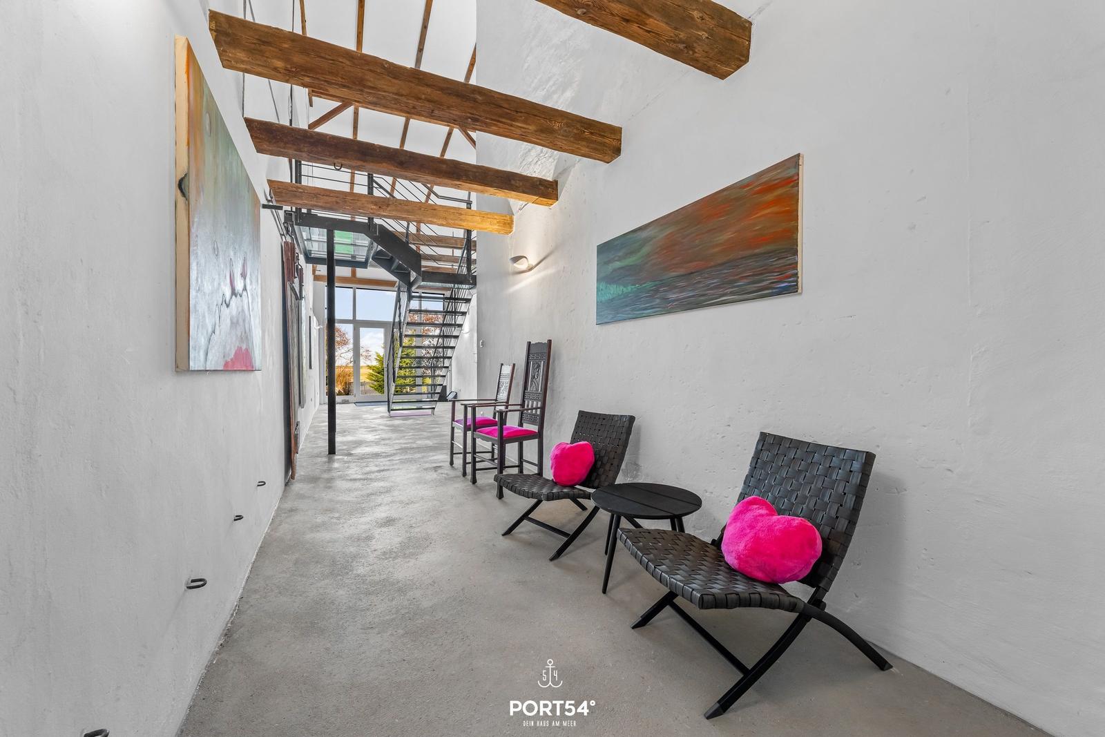 Langgezogene Halle mit Sitzgelegenheiten und Holzbalken an der Decke.