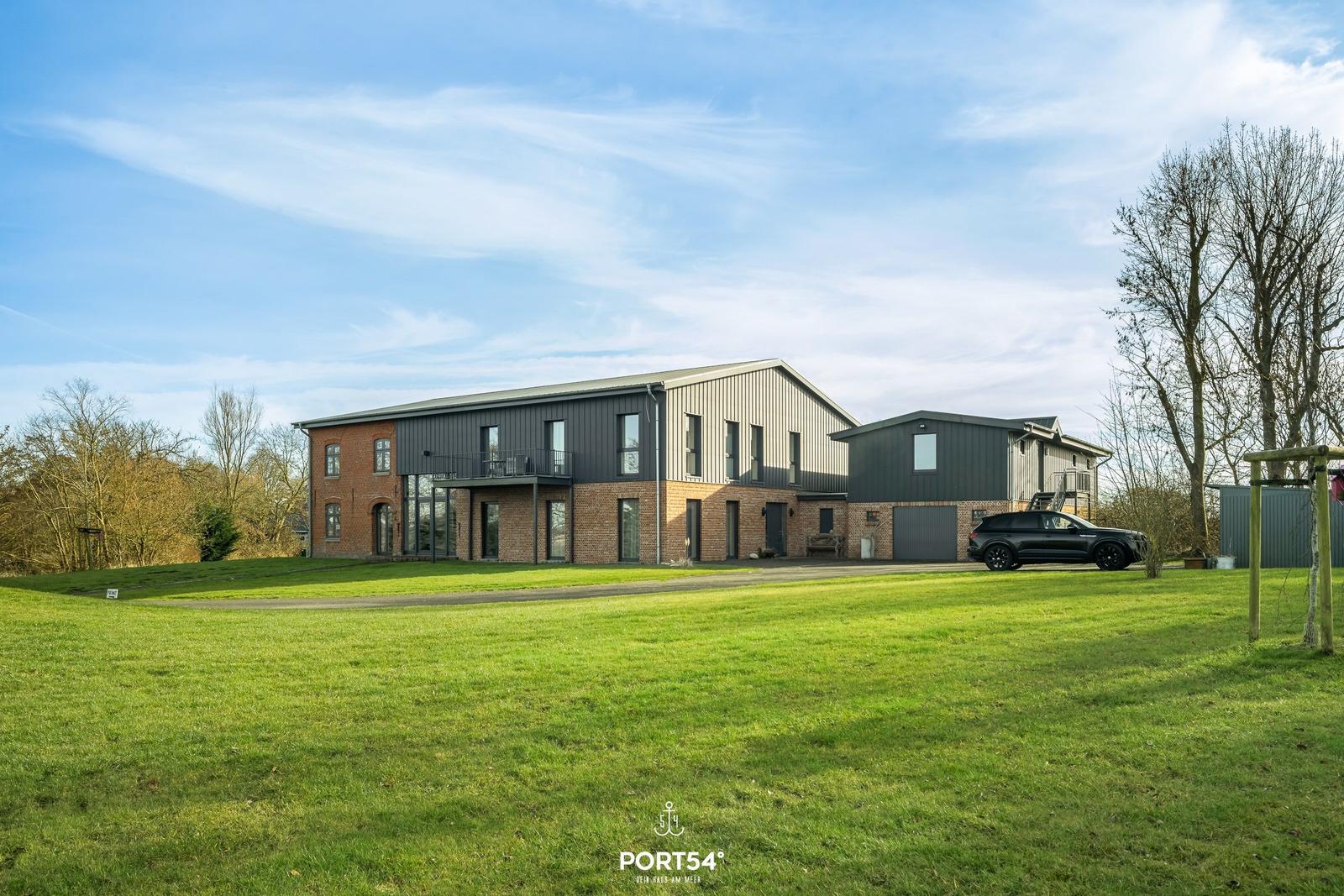 Modernes Haus mit großem Garten und Parkplatz. Ein schwarzes Auto steht vor dem Gebäude.