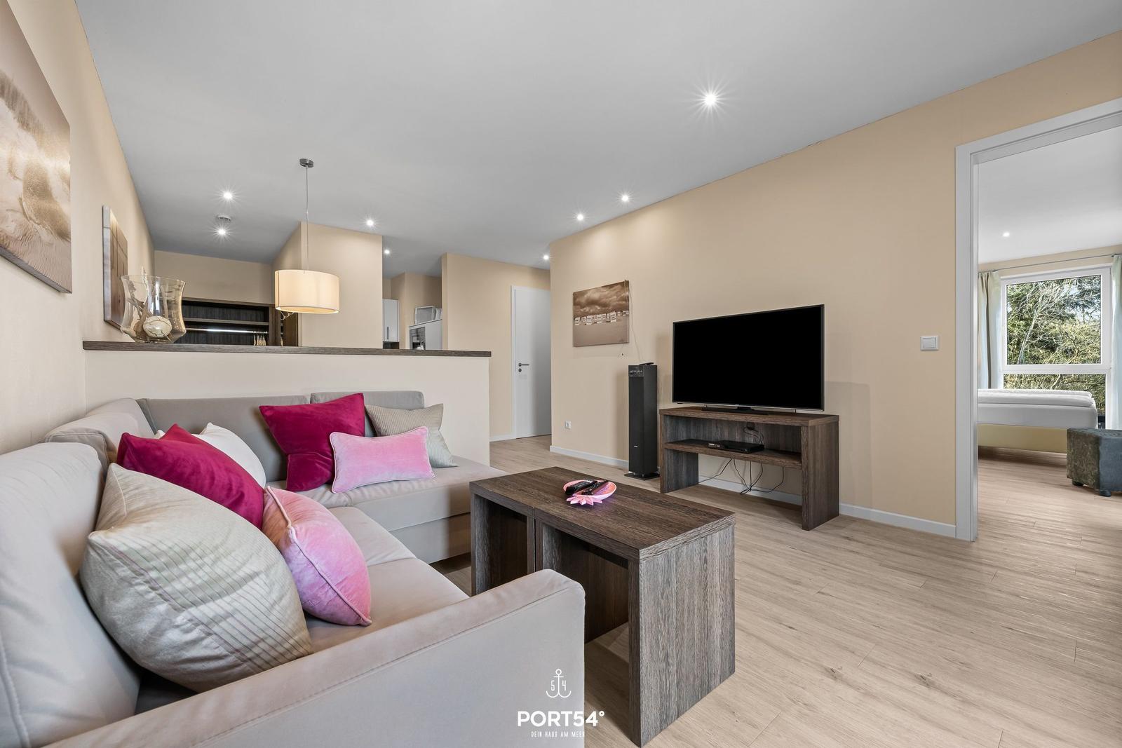 Wohnzimmer mit Sofa, Fernseher und Blick in Schlafzimmer.