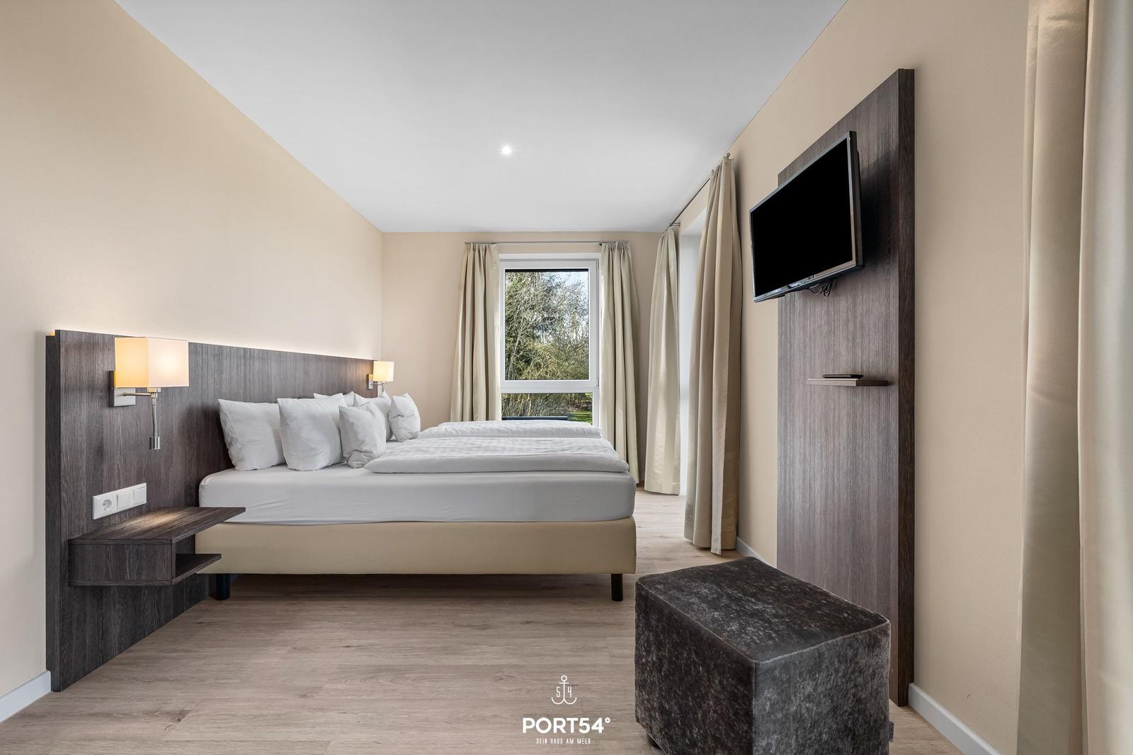 Schlafzimmer mit Doppelbett, TV und Fenster mit Blick auf Garten.