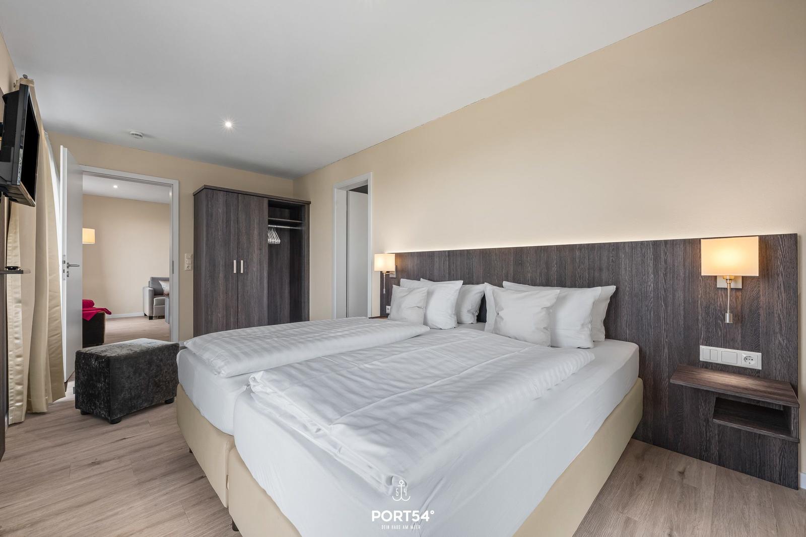 Doppelbett mit weißen Bettwäsche, Nachttische und Kleiderschrank.