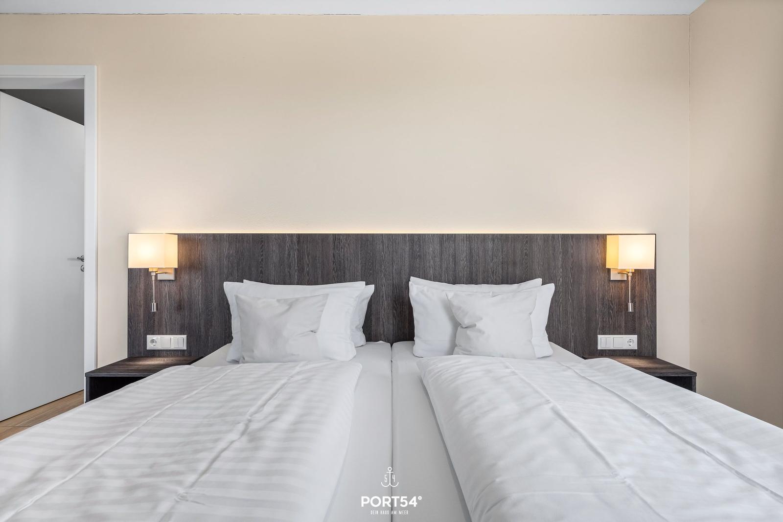 Zwei Betten mit weißen Bettwäschen und Nachttischen mit Lampen.