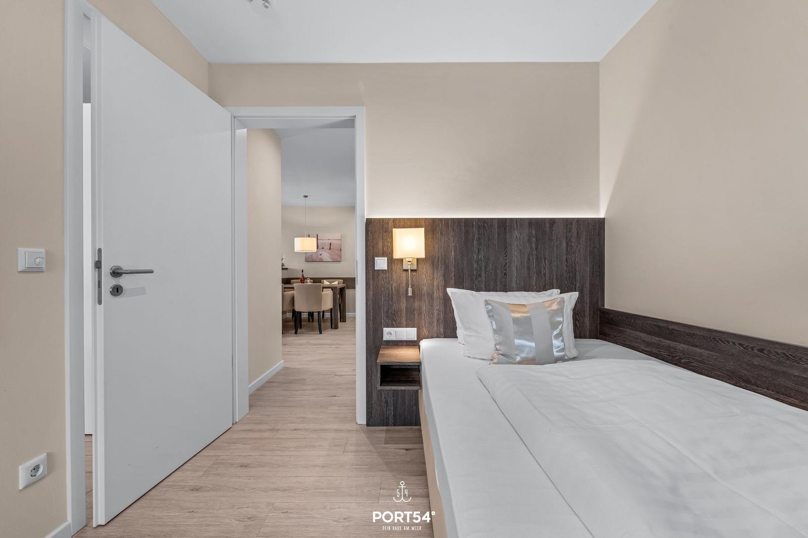 Schlafzimmer mit Bett und Holzpaneelen. Durchgang zum Essbereich mit Tisch und Stühlen.