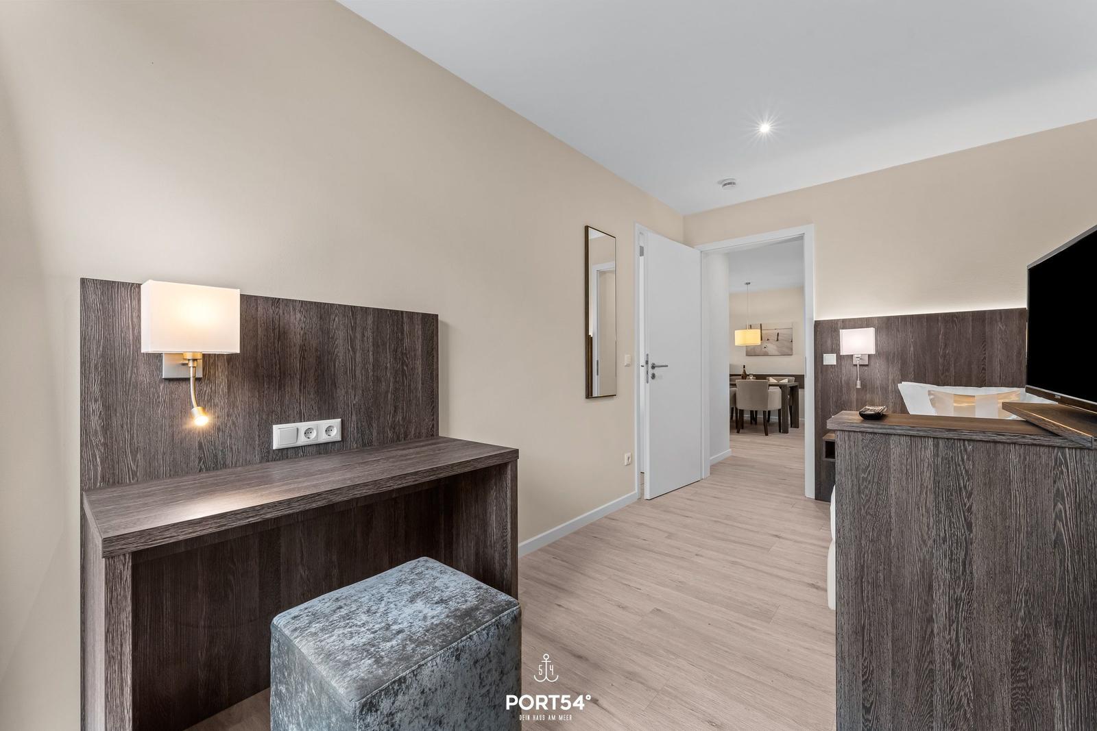 Schlafzimmer mit Schreibtisch und Fernseher. Durchgang zur Küche.