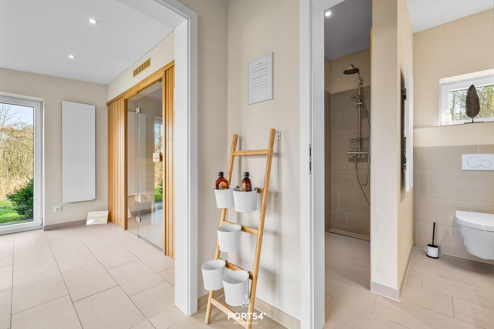 Badezimmer mit Dusche, Toilette und Holzregal mit Flaschen.