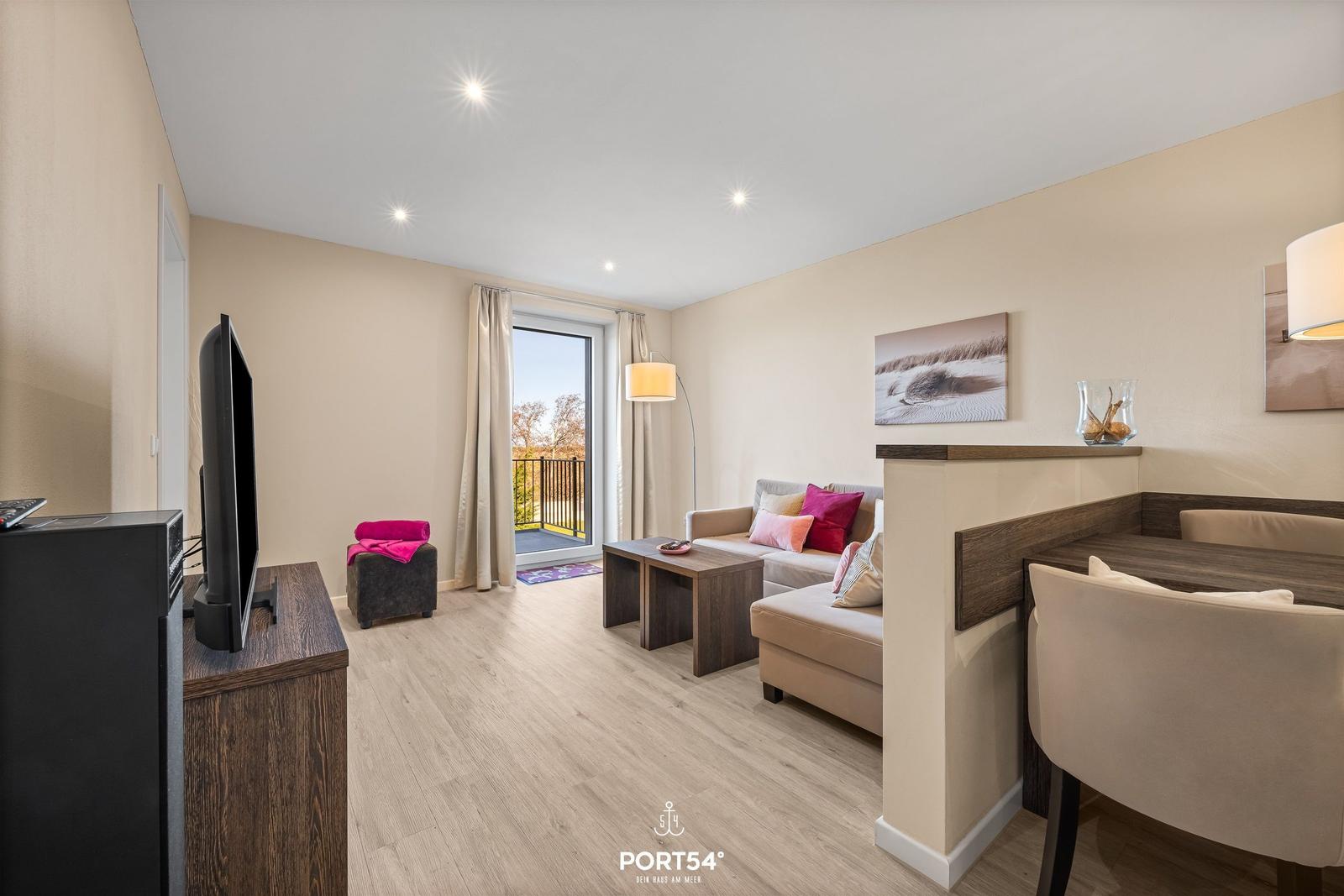 Wohnbereich mit Sofa, TV und Balkonansicht.