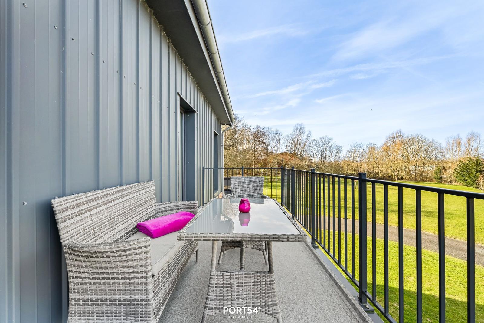 Terrasse mit Sitzgruppe und Tisch, Blick auf grünen Rasen und Bäume.