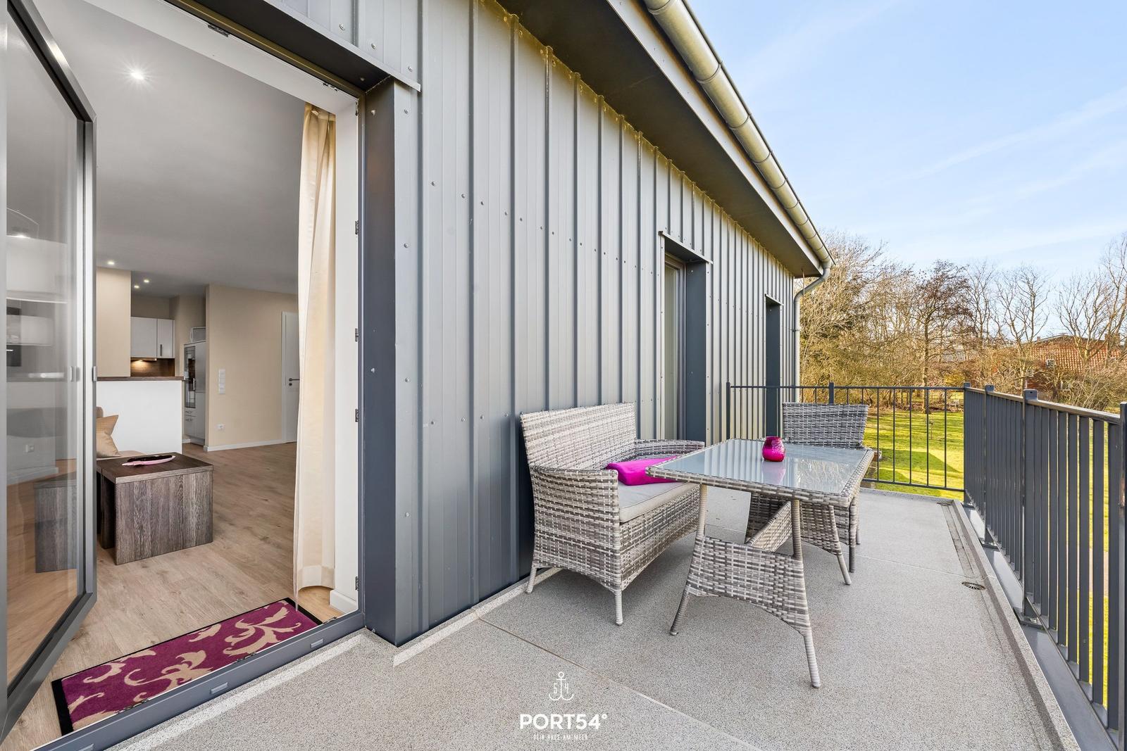 Terrasse mit Sitzgruppe und Blick auf Grünfläche. Durchgang ins Innere mit Küchenbereich.