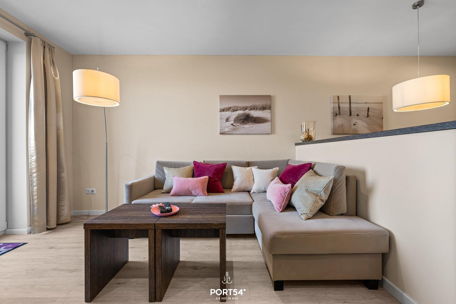 Wohnzimmer mit Ecksofa, Tisch und Wandbildern.